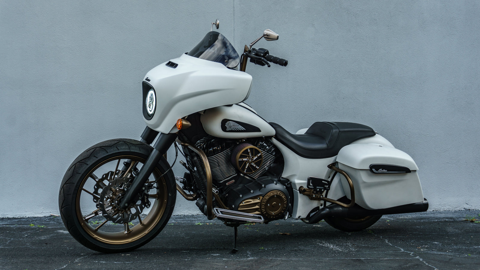 A matte white Indian Chieftain motorcycle with bronze wheels parked against a plain gray wall