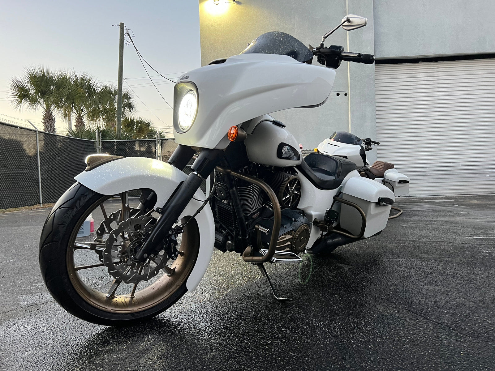 A white Indian motorcycle with bronze wheels parked outdoors with its headlight on.